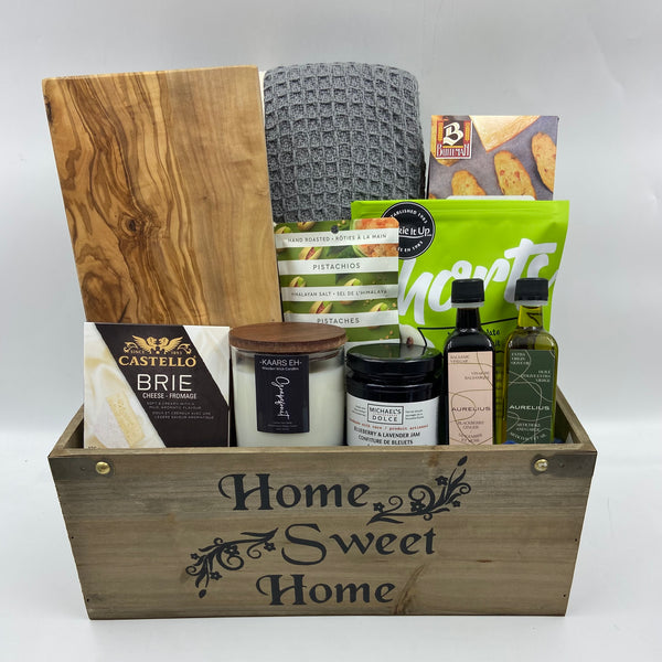 Part of our everyday collection, the Home Haven Gift Basket offers the perfect blend of comfort and flavor for any occasion. Nestled in a charming wooden container with “Home Sweet Home” on the front, this thoughtful selection features a cozy blanket, acacia cutting board, savory cheese, locally crafted spread, crackers, all-natural candle, gourmet nuts, handmade shortbread, and a pairing of infused olive oil and balsamic vinegar. It’s an invitation to relax, indulge, and enjoy a taste of home.